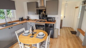 A modern kitchen with grey cabinets, a stainless steel range hood, a built-in oven, and a compact refrigerator. - Pear Tree Lodge (Alford)
