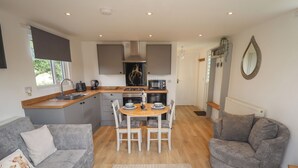 A compact living space with a kitchenette, a dining area, and a seating area with a sofa and armchair. - Pear Tree Lodge (Alford)