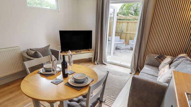A modern living room with a dining table, sofa, and TV. - Pear Tree Lodge (Alford)