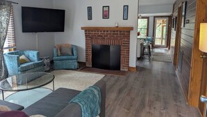 Ein Wohnzimmer mit Kamin, Fernseher und Essbereich mit Blick ins Freie.