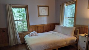 Ein Bett mit Holzrahmen, weiße Bettwäsche und Kissen, ein Nachttisch und ein gerahmtes Bild an der Wand.