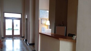 Een hotel receptie met een incheckbalie, een receptiebalie, een bord aan de muur en een deur naar buiten.