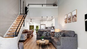 A spacious living area with a staircase, grey sofas, a round coffee table, and a kitchen in the background. - Dobie 24 with Wintergreen Advantage (Wintergreen)