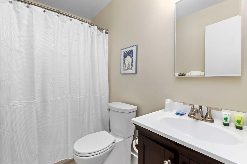 A bathroom with a white toilet, a shower curtain, a sink with a mirror above it, and toiletries on the sink.