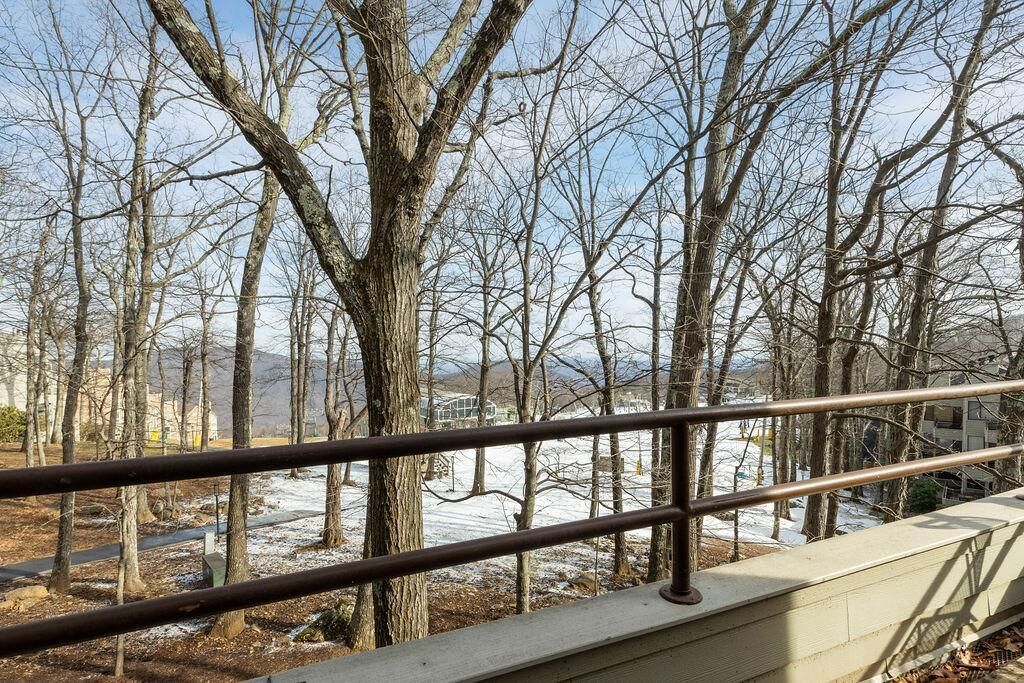 A view from a balcony with a metal railing, overlooking a snow-covered landscape with bare trees and distant buildings.