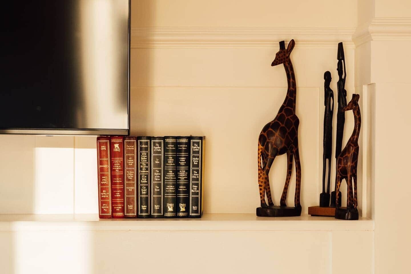 A bookshelf with books and a giraffe sculpture.