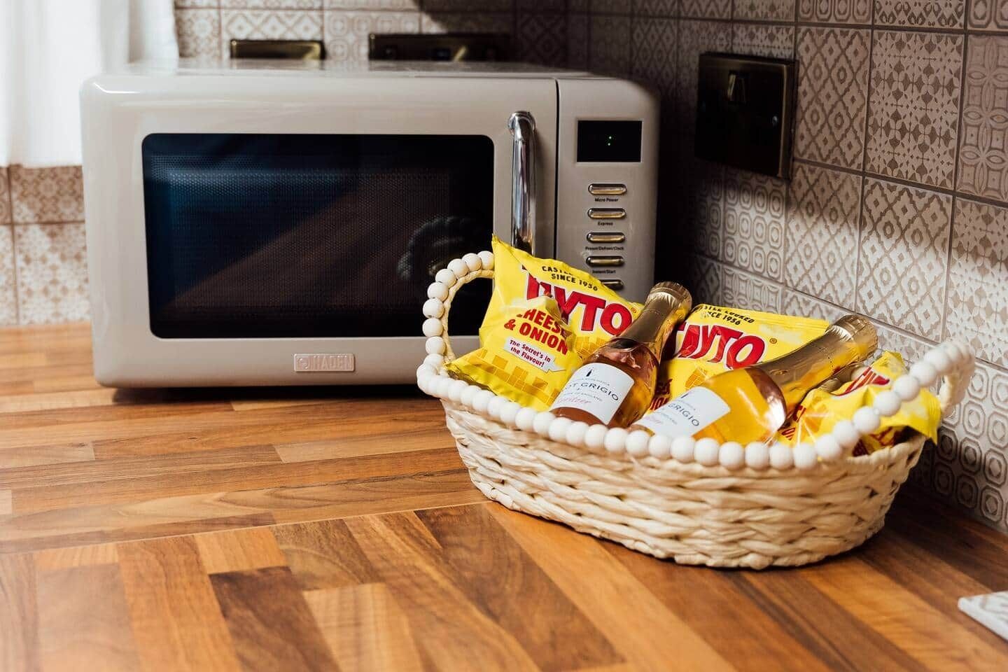 Een magnetron en een mand met etenswaren op een houten aanrecht.