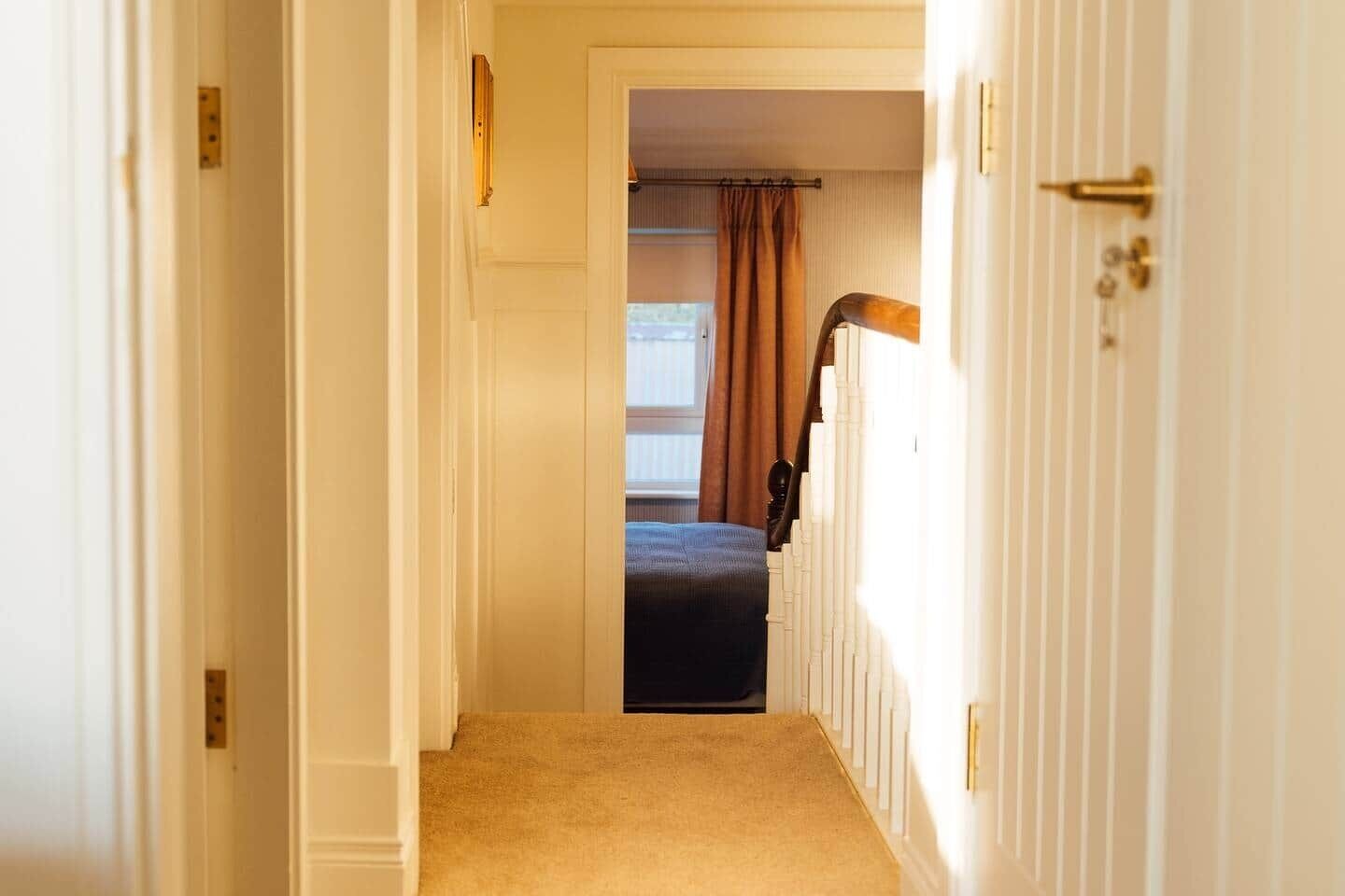 Un couloir étroit mène à une chambre qui contient un lit, un radiateur et une porte dotée d’une poignée.