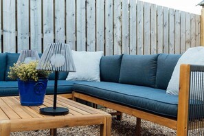 Un sofá azul con cojines blancos, una mesa de madera y una maceta azul con una planta.