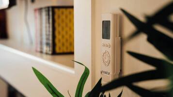 A thermostat on a wall, a bookshelf with books, and a plant.