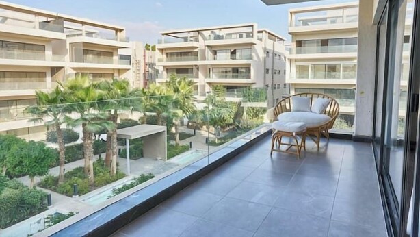 Um edifício de apartamentos moderno com uma varanda, apresentando uma cadeira de vime e uma pequena mesa.