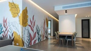 Uma sala de estar moderna com mesa de pingue-pongue, área de jantar com mesa e cadeiras de madeira e um mural colorido na parede.