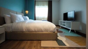 Quarto moderno com uma cama grande, televisão e uma mesa de cabeceira branca.