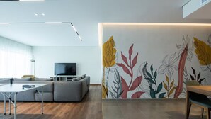 Uma sala moderna com um sofá cinza, uma televisão, uma mesa de jantar e um mural de parede colorido.