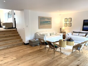 Ett modernt vardagsrum med en vit soffa, flätade stolar, ett soffbord och en tavla på väggen.