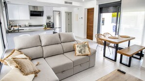 Una sala de estar moderna con un sofá seccional gris, una mesa de centro de madera y un comedor con una mesa y sillas de madera.