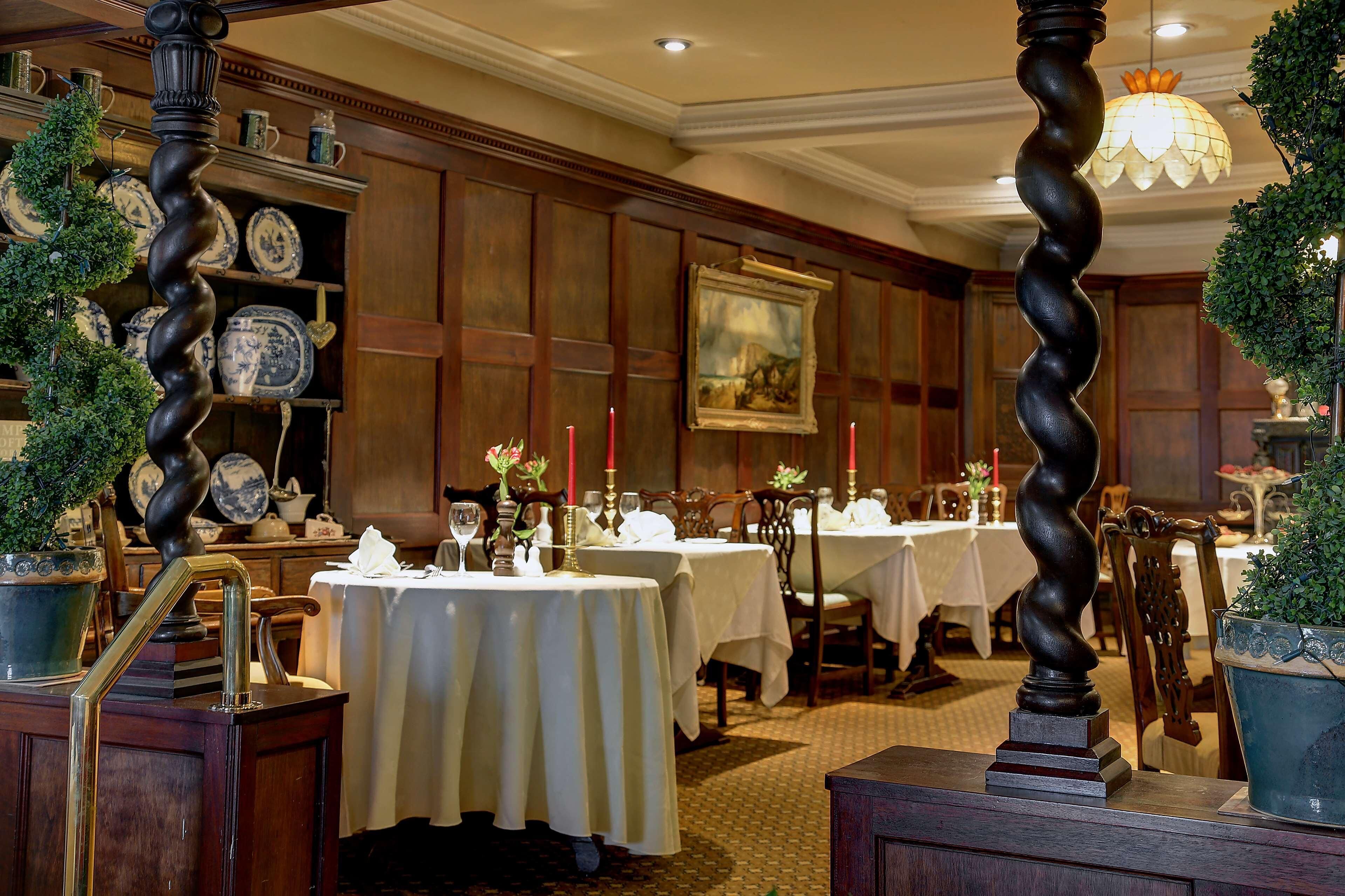 A dining area with tables set for service, wooden paneling, and a chandelier.