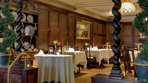 Une salle à manger avec des tables dressées, des boiseries et un lustre.