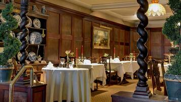 A dining area with tables set for service, wooden paneling, and a chandelier.