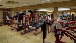 Une salle de sport équipée de divers appareils d’exercice, dotée de planchers en bois et d’un mur recouvert de miroirs.