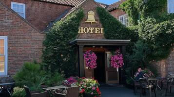 A hotel entrance with a bell sign, brick facade, and outdoor seating area with potted plants.