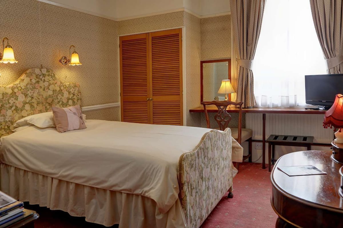 A hotel room with a bed, a desk with a lamp, a television, and a wardrobe.