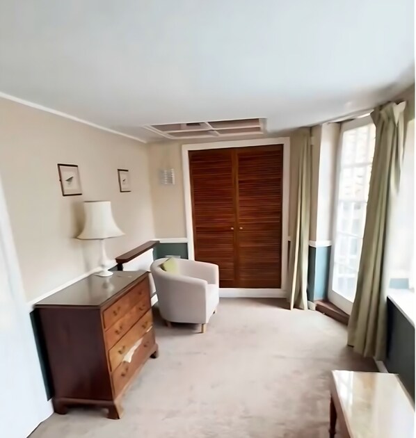 Une chambre à coucher avec une commode en bois, une chaise, une table de chevet, une armoire et une fenêtre avec des rideaux.