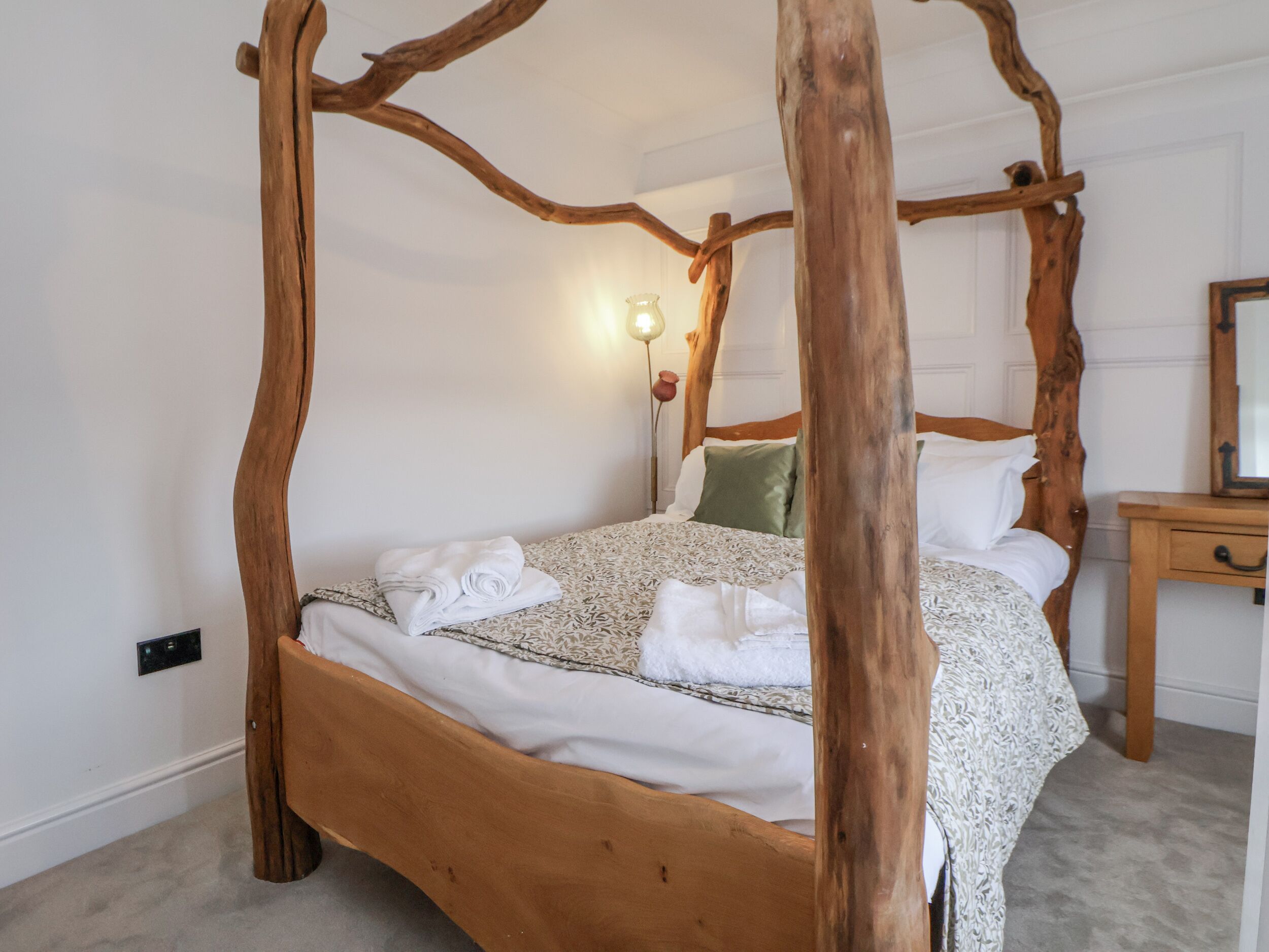 Una cama con dosel de madera, una mesita de noche con lámpara y un espejo en la pared.