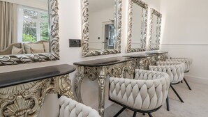 Una habitación con espejos de plata ornamentados, un sofá con cojines color crema y sillones tapizados.