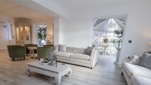 Un salón espacioso con un sofá color beige, una mesa de centro y dos sillones. Se aprecia un comedor al fondo.