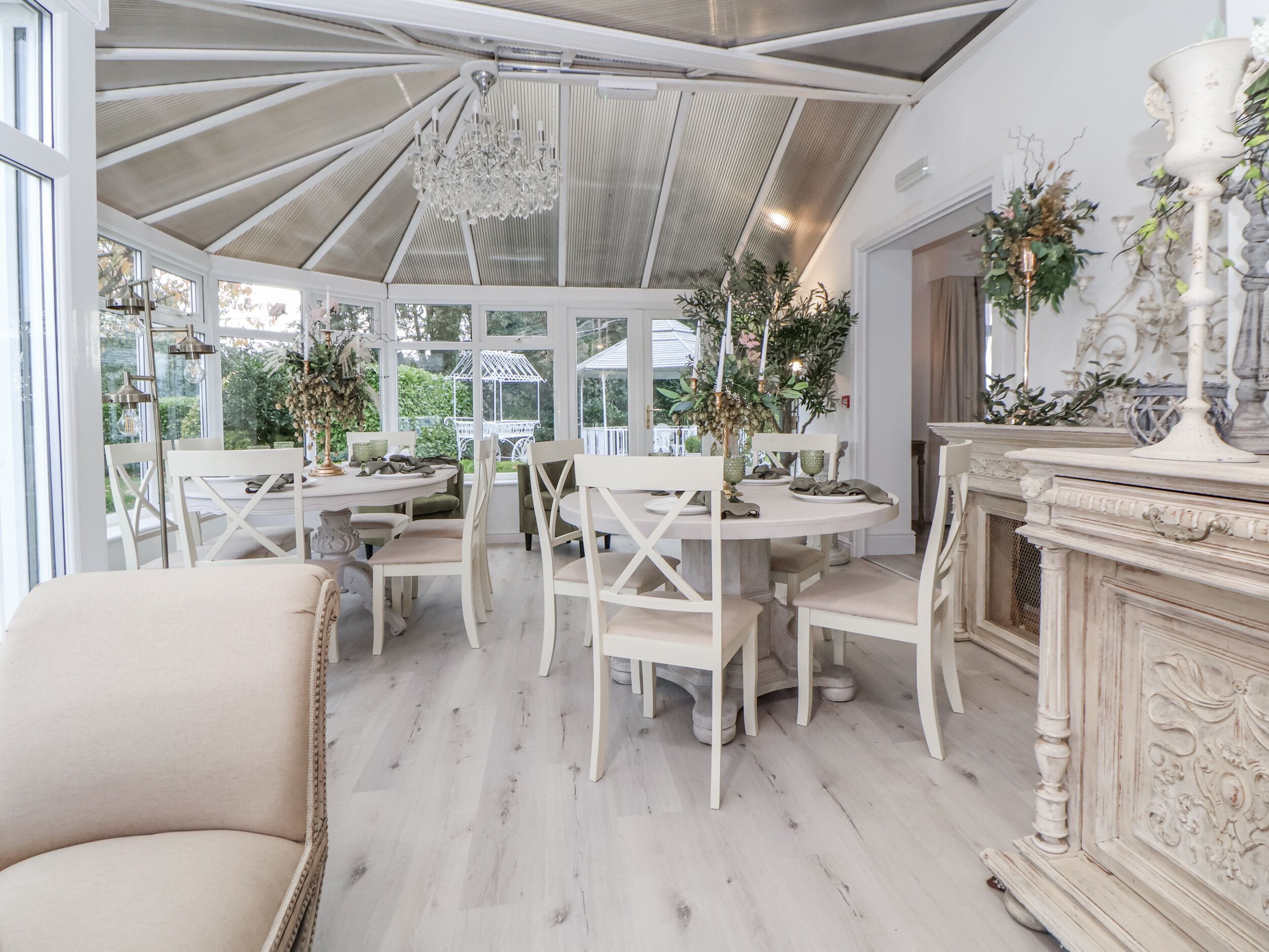 A conservatory with a high ceiling, white furniture, and a fireplace.