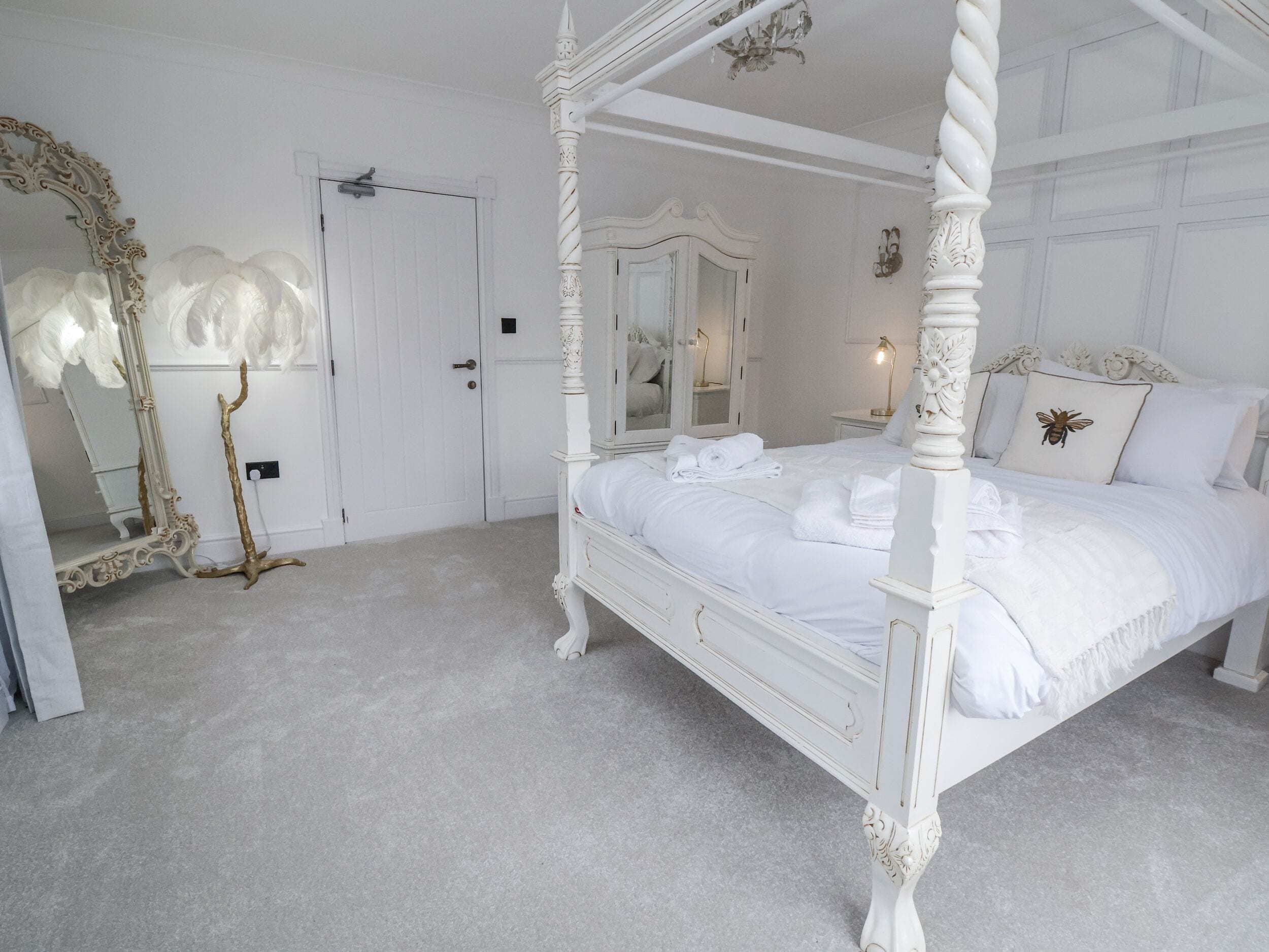Un lit à baldaquin blanc, avec un miroir et une commode, dans une chambre à coucher.