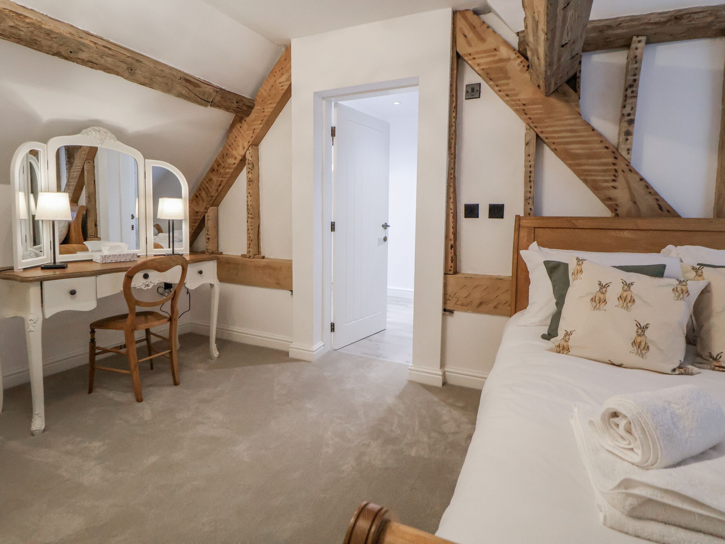 A bedroom with a wooden bed, a desk with a mirror, and a door leading to another room.