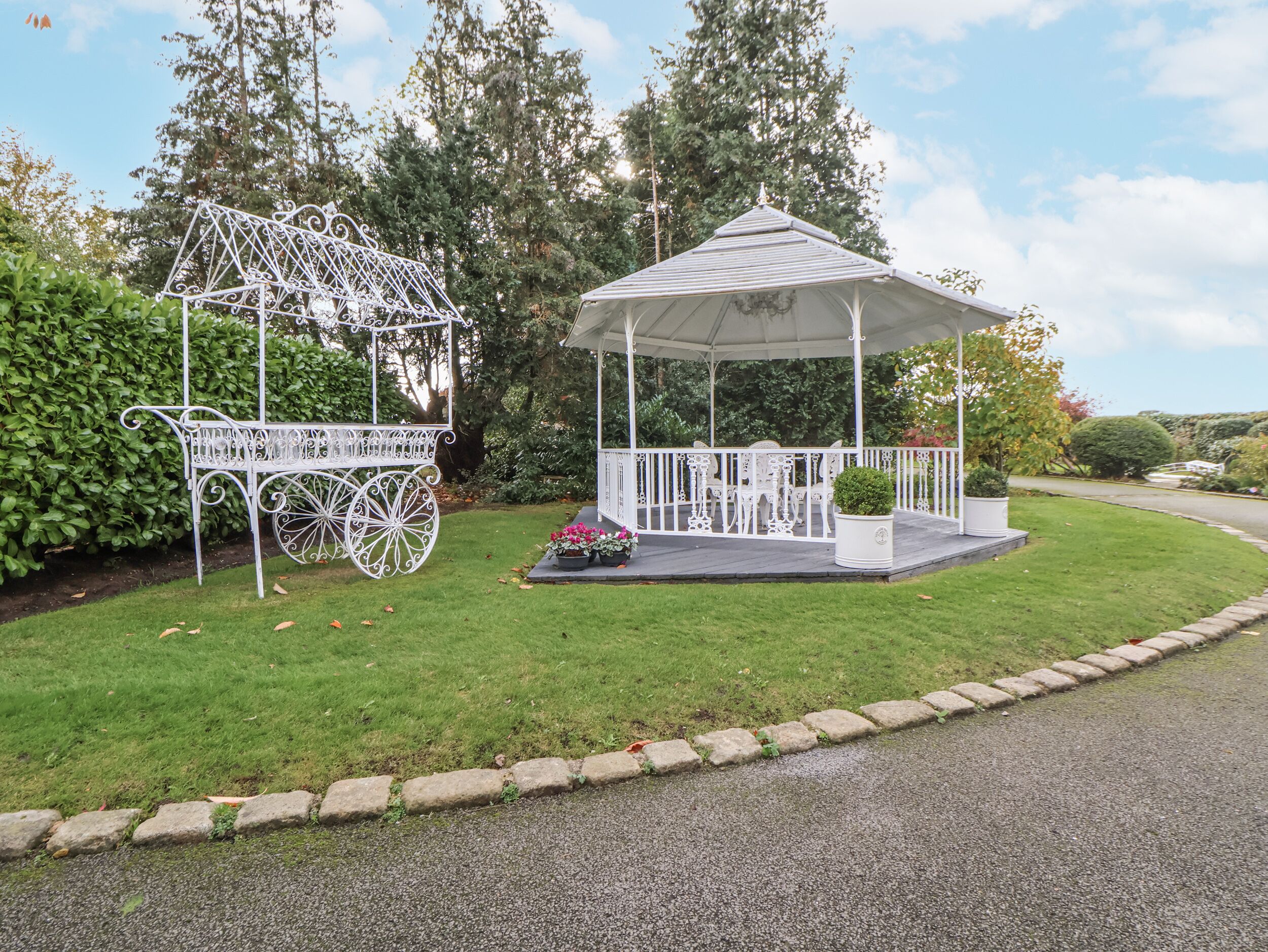 A gazebo with a white railing and a white carriage-like structure with intricate metalwork.