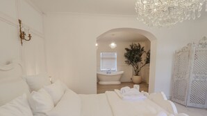 Un dormitorio amplio con una cama grande, un candelabro y vistas al baño a través de un arco.