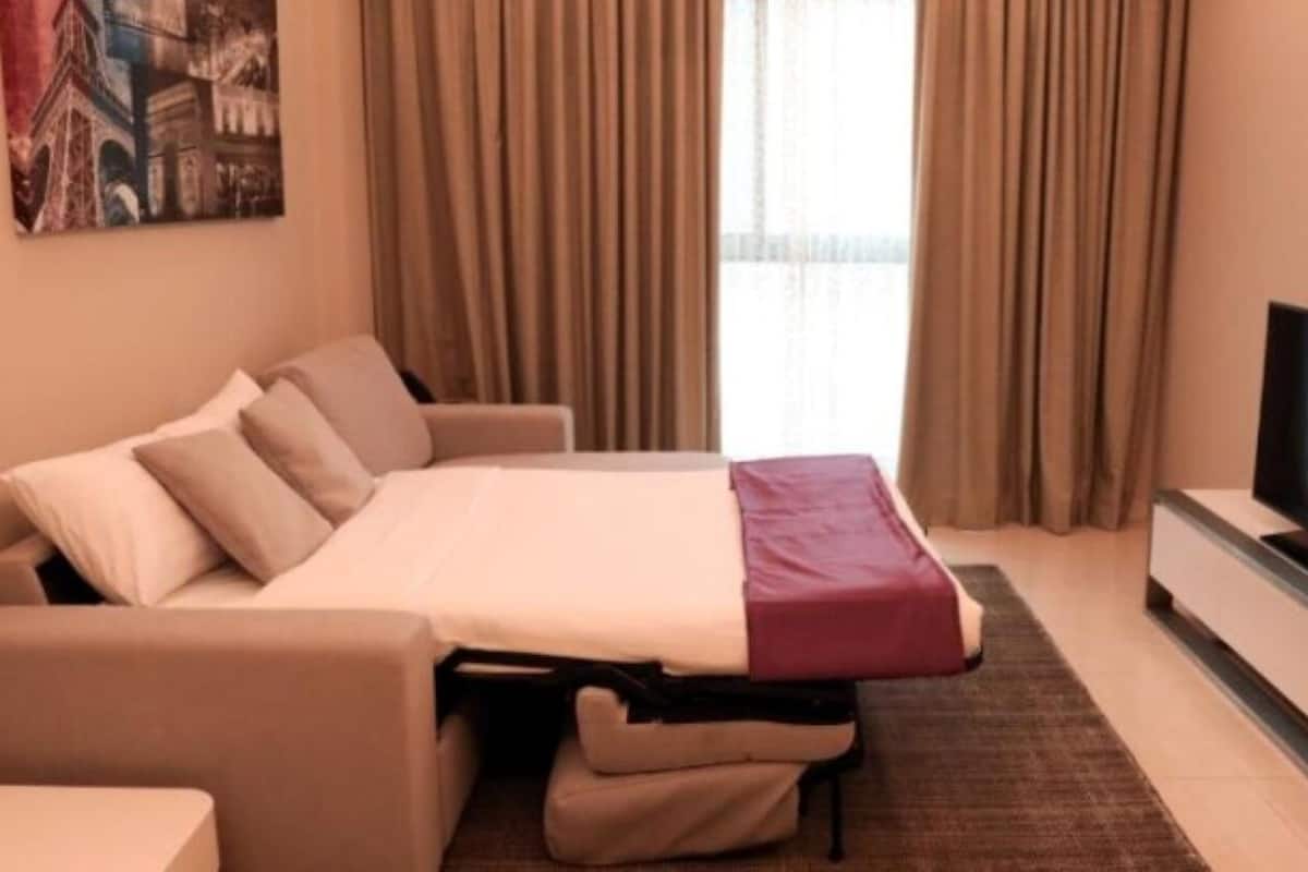 A hotel room with a sofa bed, a flat-screen TV, and a painting on the wall.