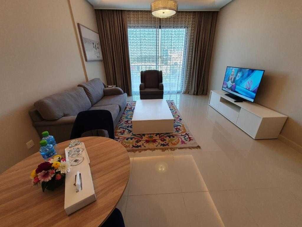 Un salon moderne avec un canapé, une table basse, un téléviseur et une table à manger agrémentée d’un vase de fleurs.