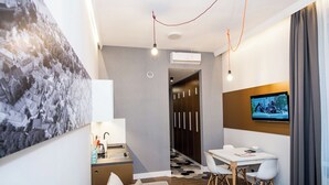 Une chambre d’hôtel moderne équipée d’un canapé, d’une table à manger avec des chaises, d’un téléviseur fixé au mur et d’un appareil de climatisation.