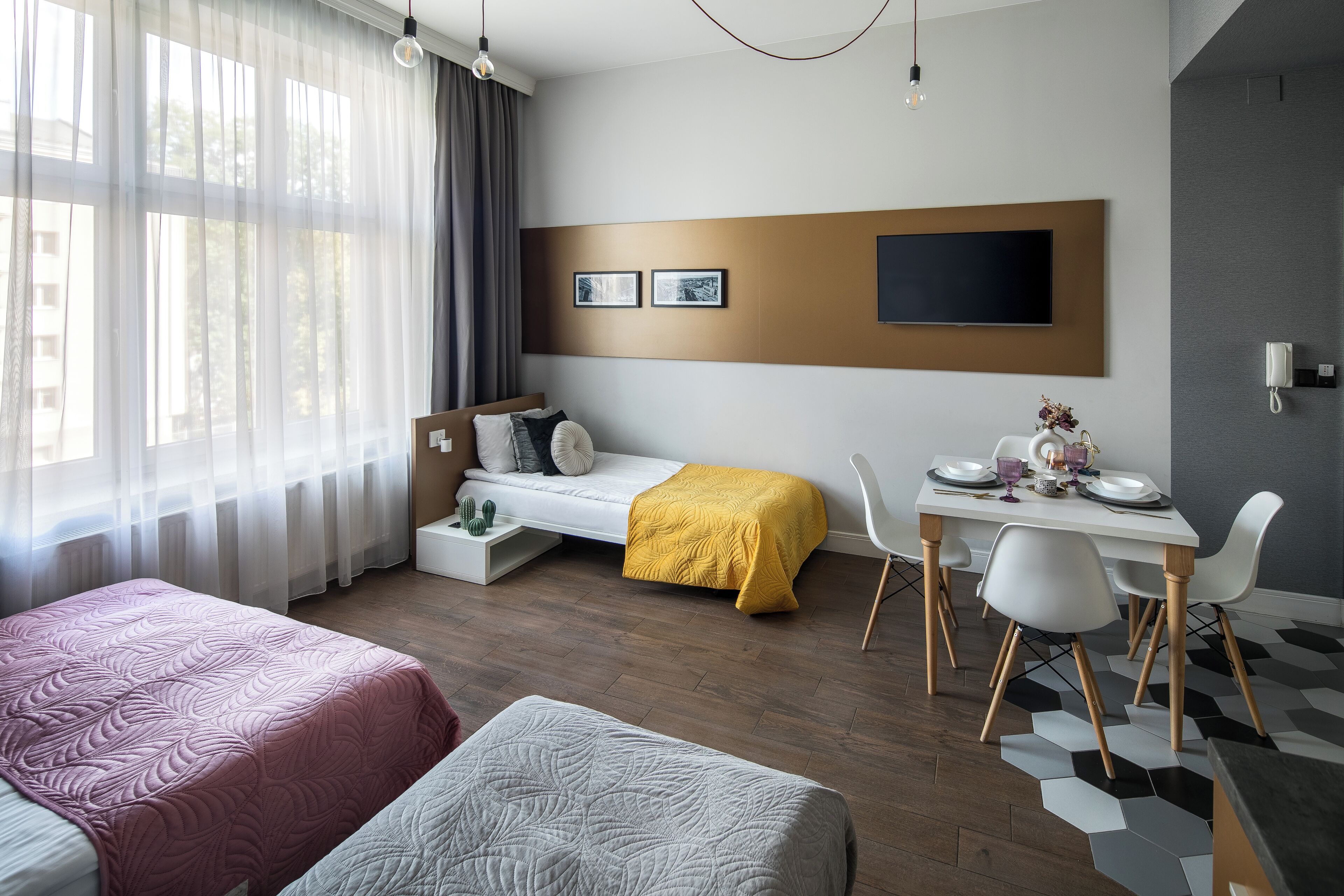 Una habitación de hotel moderna con una cama, un sofá, un comedor con mesa y sillas, y un televisor montado en la pared.