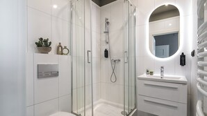 Une salle de bain moderne avec une douche à parois de verre, des toilettes blanches et un meuble-lavabo avec un miroir.