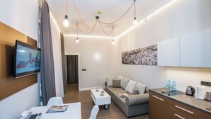 Un espace de vie moderne et compact, doté d’un téléviseur à écran plat, d’un canapé, d’un petit coin cuisine et d’une table à manger.