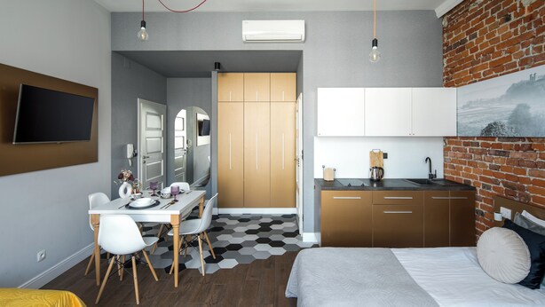 Une chambre d’hôtel moderne équipée d’un lit, d’un bureau avec des chaises, d’une kitchenette et d’un téléviseur fixé au mur.
