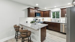 A modern kitchen with dark wood cabinets, a granite countertop, stainless steel appliances, and a large window providing natural light. - The White House | Unit 3 (Shaver Lake)