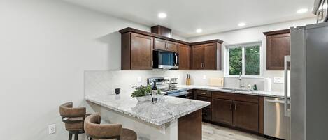 A modern kitchen with dark wood cabinets, a granite countertop, stainless steel appliances, and a large window providing natural light.