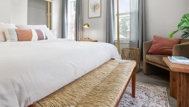 A modern bedroom with a large bed, a bench, a sofa, and a small side table.
