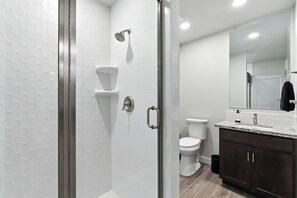 A modern bathroom with a glass-enclosed shower, a white toilet, and a dark wooden vanity with a marble countertop. - The White House | Unit 4 Game Room (Shaver Lake)