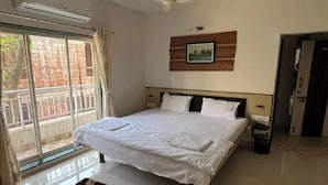 Un dormitorio con una cama, un ventilador de techo, un cuadro colgado en la pared y una ventana con vista a un muro de ladrillos.