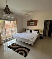 Un dormitorio con cama, ventilador de techo, ventana con cortinas y una puerta.