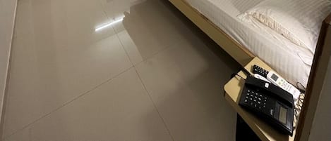 A hotel room with a bed, a ceiling fan, an air conditioning unit, a television, and a telephone on a bedside table.