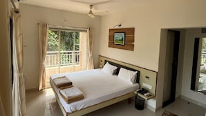 Habitación de hotel con una cama grande, un ventilador de techo, una ventana con cortinas y una mesita de noche pequeña.